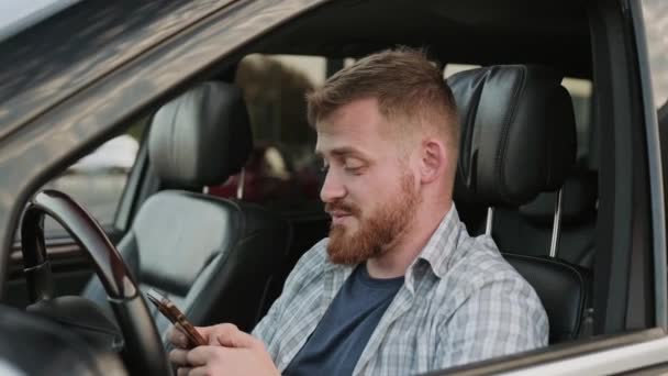 スマートフォンでタイピングしながら運転席に座っている若い男 トランスポート テクノロジー 旅行コンセプト スローモーション — ストック動画