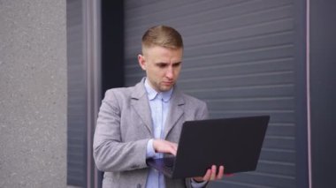 İş adamı dışarıda iş arkadaşına el sallarken dizüstü bilgisayarda yazı yazmakla meşgul. İş, teknoloji kavramı. Gerçek zamanlı.