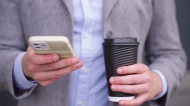 İş adamı cep telefonunda yazarken elinde sıcak bir içecek tutuyor. Kapatın. İş, iş, teknoloji konsepti. Gerçek zamanlı.