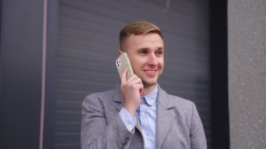 Açık havada kahvenin tadını çıkarırken akıllı telefondan konuşan genç ve mutlu bir iş adamı. İş, iş, teknoloji konsepti. Gerçek zamanlı.