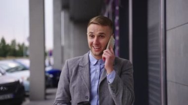 Şehirde yürürken elinde kahve tutarak akıllı telefondan konuşan genç ve mutlu bir işadamı. İş, teknoloji kavramı. Gerçek zamanlı.