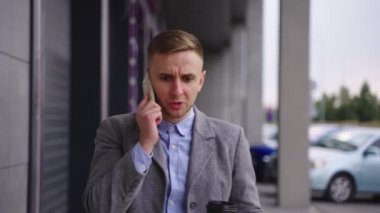 Kızgın işadamı dışarıda yürürken kahve tutuyor ve cep telefonuyla konuşuyor. İş, iş, teknoloji konsepti. Gerçek zamanlı.