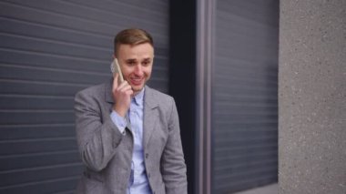 Dışarıda dikilen ve cep telefonuyla konuşan mutlu genç işadamı başarıyı kutluyor. İş, teknoloji kavramı. Gerçek zamanlı.