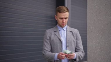 Genç adam dışarıda duruyor ve para sayıyor, cebine koyuyor. Uzayı kopyala İş, ödeme konsepti. Gerçek zamanlı.