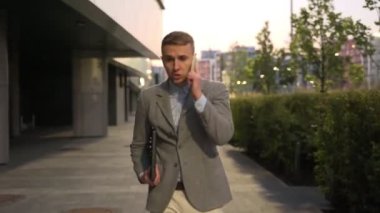 İşadamı cep telefonuyla konuşurken dizüstü bilgisayar tutuyor, cadde boyunca yürüyor. İş, iş, teknoloji konsepti. Gerçek zamanlı.