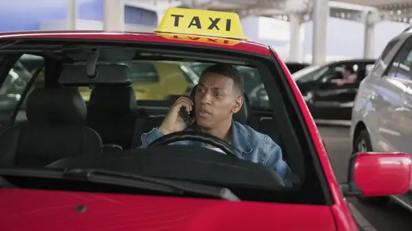 Upset African American taxi driver talking on the mobile phone. Yellow taxi car roof sign. People, job, service concept. Slow motion