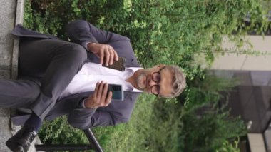 Mutlu iş adamı kahveyle eğleniyor, telefon kullanıyor, dışarıda oturuyor. İş, iletişim, teknoloji konsepti. Yavaş çekim