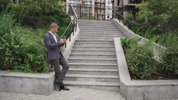 Ευτυχισμένος Επιχειρηματίας Κρατώντας Smartphone Ποζάροντας Κοντά Σκαλοπάτια Στην Πόλη Επιχείρηση — Αρχείο Βίντεο