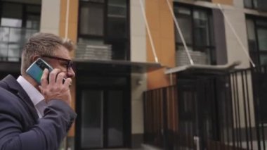 Sokakta yürürken gözlüklü bir işadamı akıllı telefondan konuşuyor. İş, iletişim, teknoloji konsepti. Gerçek zamanlı konsept