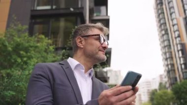 Şehirde akıllı telefon kullanan gözlüklü mutlu bir iş adamı. İş, iletişim, teknoloji konsepti. Gerçek zamanlı konsept