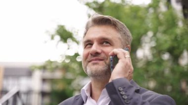 Olumlu yetişkin iş adamı telefonda konuşurken dışarıda duruyor. İş, iletişim, teknoloji konsepti. Gerçek zamanlı konsept