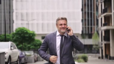 Şehirde yürürken cep telefonu tutan ve konuşan mutlu yetişkin iş adamı. İş, insanlar, teknoloji kavramı. Gerçek zamanlı konsept