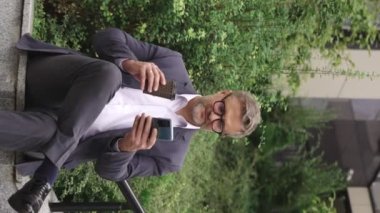 Mutlu iş adamı kahveyle eğleniyor, telefon kullanıyor, dışarıda oturuyor. İş, iletişim, teknoloji konsepti. Gerçek zamanlı konsept