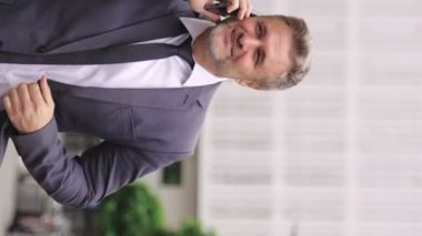 Gülümseyen iş adamı cep telefonuyla konuşurken şehirde yürüyor. İş, teknoloji, insan kavramı. Gerçek zamanlı konsept