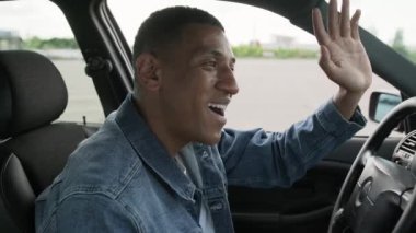 Gülümseyen Afrikalı Amerikalı taksi şoförü el sallıyor, arabayı sürüyor. Servis arabası konsepti. Yavaş çekim