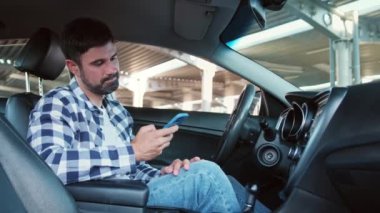 Genç bir adam akıllı telefonu tutarken arabada oturmuş, ekrana bakıyor. Ulaşım, teknoloji, yaşam tarzı konsepti. Yavaş çekim