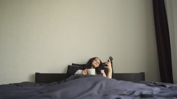 Mulher Preguiçosa Segurando Telefone Celular Xícara Café Enquanto Estava Deitada — Vídeo de Stock