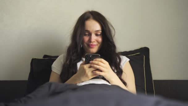 Lächelt Hübsch Weiblich Mit Dem Smartphone Während Sie Hause Bett — Stockvideo