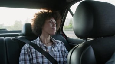 Bir arabanın arka koltuğunda oturan Afro-Amerikalı genç bir kadın ve camdan dışarı bakıyor. Ulaşım, yaşam tarzı. İnsanlar konsepti. Yavaş çekim