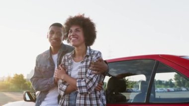 Gülümseyen genç adam dışarıda arabaya yaslanırken bir kadına sarılıyor. Ulaşım, seyahat, ilişki, insan konsepti. Yavaş çekim