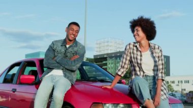 Gülümseyen Afro-Amerikan kadın arabanın kaputunda oturmuş dışarıdaki adama bakıyor. Ulaşım, seyahat, ilişki, insan konsepti. Yavaş çekim