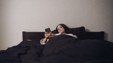 Evdeki yatak odasında uyumadan önce akıllı telefon kullanan ve sohbet eden genç bir kadın. Ağır çekim. Yaşam tarzı kavramı