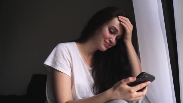 Mulher Sorridente Usando Telefone Celular Enquanto Descansa Perto Janela Sala — Vídeo de Stock