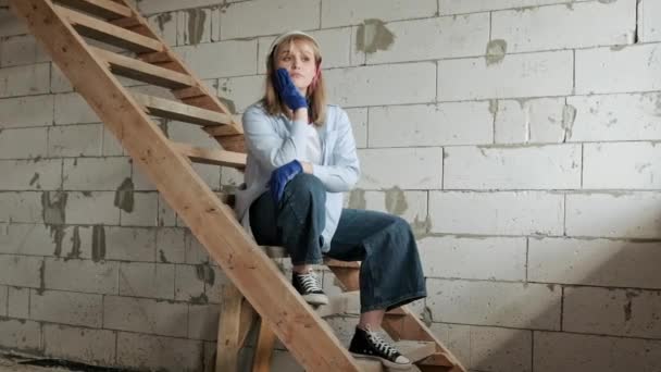 Zamyślony Pracownik Budowlany Siedzący Drewnianych Schodach Pod Białą Ceglaną Ścianą — Wideo stockowe