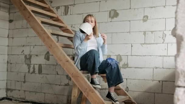 Müde Bauarbeiterin Sitzt Auf Holztreppen Vor Weißer Backsteinmauer Nimmt Schutzhelm — Stockvideo