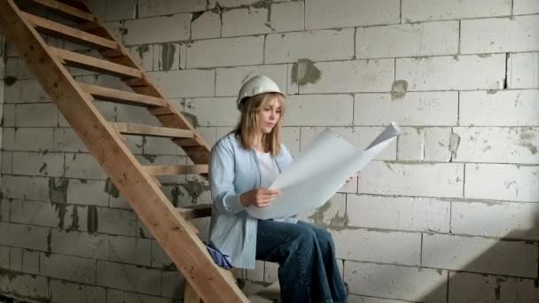 Εστιασμένη Γυναίκα Αρχιτέκτονας Σκληρό Καπέλο Κάθεται Σκάλες Ημιτελείς Κατοικίες Αναλύοντας — Αρχείο Βίντεο