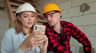 İnşaat işçisi, henüz tamamlanmamış bir binada olan meslektaşına cep telefonuyla bir şeyler gösterirken gülümsüyor. Yavaş çekim