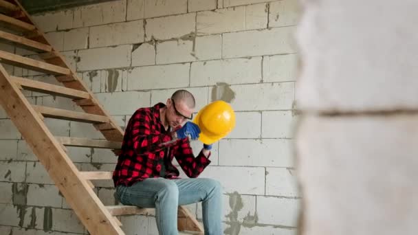 Erschöpfter Bauarbeiter Sitzt Auf Einer Treppe Vor Einer Ziegelmauer Und — Stockvideo