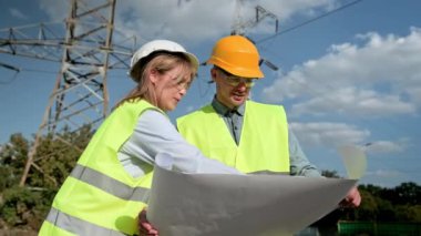 Elektrik hattı müfettişi, olay yerinde yapılan denetim sırasında iletim kulesinin önünde çizimlerle ilgili bir şey gösteriyor. Yavaş çekim