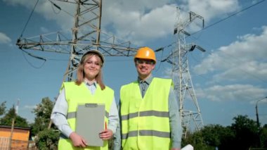 Gülümseyen elektrik hattı müfettişleri ve şantiye teftişi sırasında şanzıman kulelerinin yanında duran çizimleri olan memnun meslektaşları. Dolly vurdu.