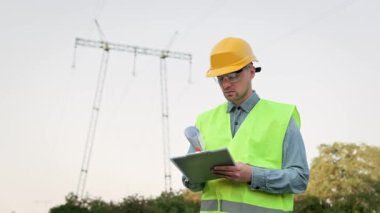 Elektrik hattı müfettişi, olay yerinde denetim sırasında elektrik direğinin yanında dururken, panonun üzerinde taslak çizimi olan bir pano. Yavaş çekim