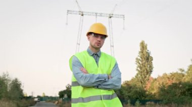 Gözlüklü enerji denetçisinin belden yukarı portresi ve denetim sırasında elektrik direğinin yanında duran sert şapka. Dolly vurdu.