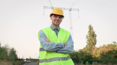 Gözlüklü ve koruyucu kasklı neşeli elektrik hattı müfettişinin belden yukarı portresi şanzıman kulesinin yanında duruyor. Dolly vurdu.