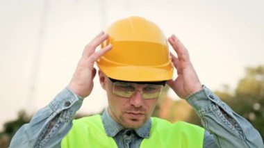 Güvenlik gözlüklü yorgun inşaat işçisinin dışarı bakarken kaskını çıkarışının yakın plan portresi. Yavaş çekim