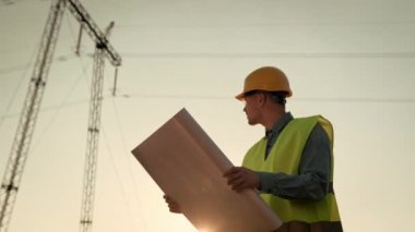 Odaklanmış güç hattı müfettişinin belden yukarı portresi çizimleri okuyor ve elektrik direğine bakıyor. Yavaş çekim