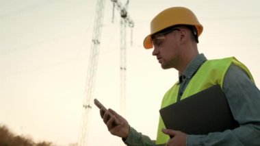 Odaklanmış güç hattı müfettişi elinde dizüstü bilgisayarla iletişim kulesinden geçerken akıllı telefon ekranına bakıyor. Yavaş çekim