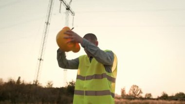 Yorgun elektrik hattı müfettişi elektrik direğinin yanında saat yönünde dönerken mutlu bir gülümsemeyle kasketini çıkartıyor. Yavaş çekim