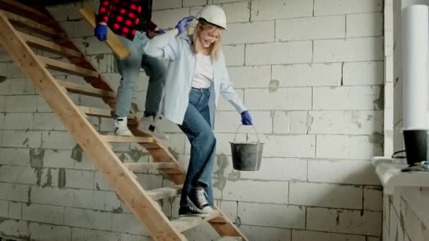 Lächelnde Bauarbeiterin Mit Eimer Die Treppen Unfertigen Wohnhaus Hinunterläuft Gefolgt — Stockvideo