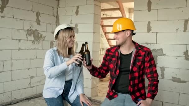 未完成の住宅ビルに座っているハードハットの笑顔の建設作業員は 飲料のボトルを凝縮しています スローモーション — ストック動画
