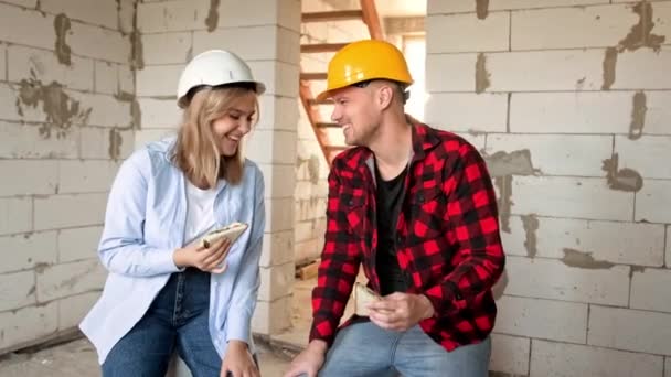 微笑的建筑商一边吃三明治 一边坐在未完工的住宅里 慢动作 — 图库视频影像