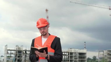 Koruyucu miğfer ve yelek giyen profesyonel bir ustabaşı defter tutuyor, not tutuyor. Yavaş çekim