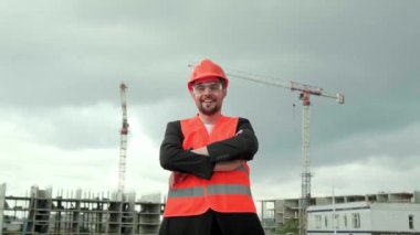 Koruyucu miğfer, yelek ve gözlüklü profesyonel müteahhit portresi sahada çalışıyor, kollarını kavuşturuyor ve gülümsüyor. Yavaş çekim