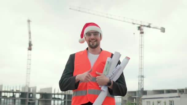 ベスト クリスマスの帽子 メガネの笑顔ビルダーは 青写真を保持し 現場で作業し 良い兆候を示しています スローモーション — ストック動画