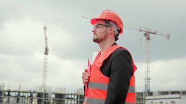 Yelekli, koruyucu kasklı ve elinde planlar olan bir erkek. Yürüme ve kontrol etme zamanı. Olay yerinde çalışıyor. Yavaş çekim
