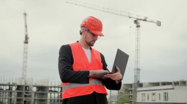 Yelekli profesyonel ustabaşı, koruyucu miğfer ve gözlük takıyor ve dizüstü bilgisayarda daktilo yazıyor. Yavaş çekim