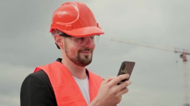 Profesyonel ustabaşının portresi koruyucu miğfer, yelek ve gözlüklü akıllı telefon ve sohbet. Yavaş çekim
